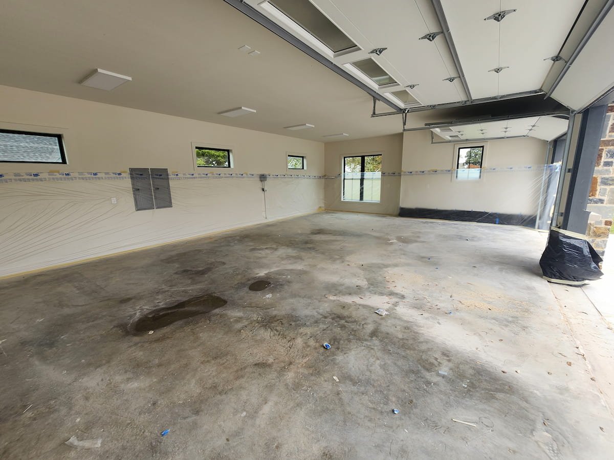 Dirty garage concrete floor with construction debris and stains before pressure washing near Richland Chambers Lake Texas