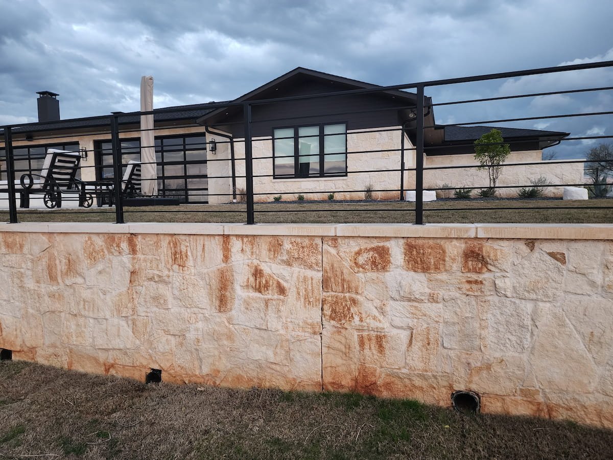 Stone retaining wall with heavy rust stains before rust removal cleaning in Streetman Texas