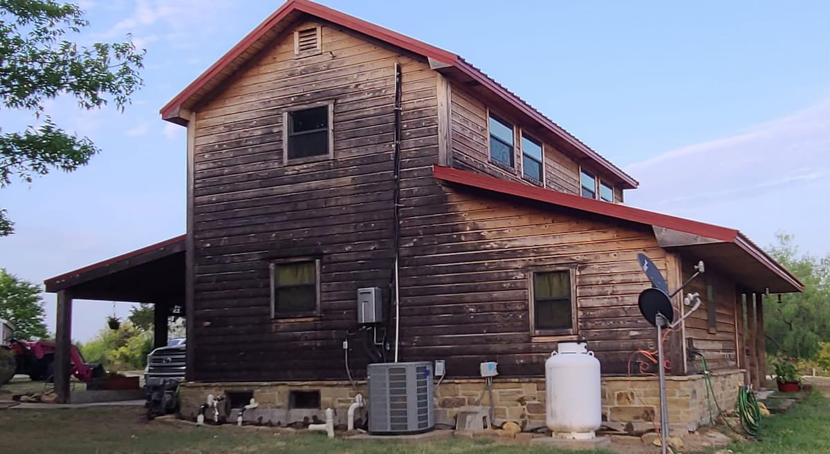 Weathered wood siding on cedar-sided home before wood restoration cleaning in Kerens Texas